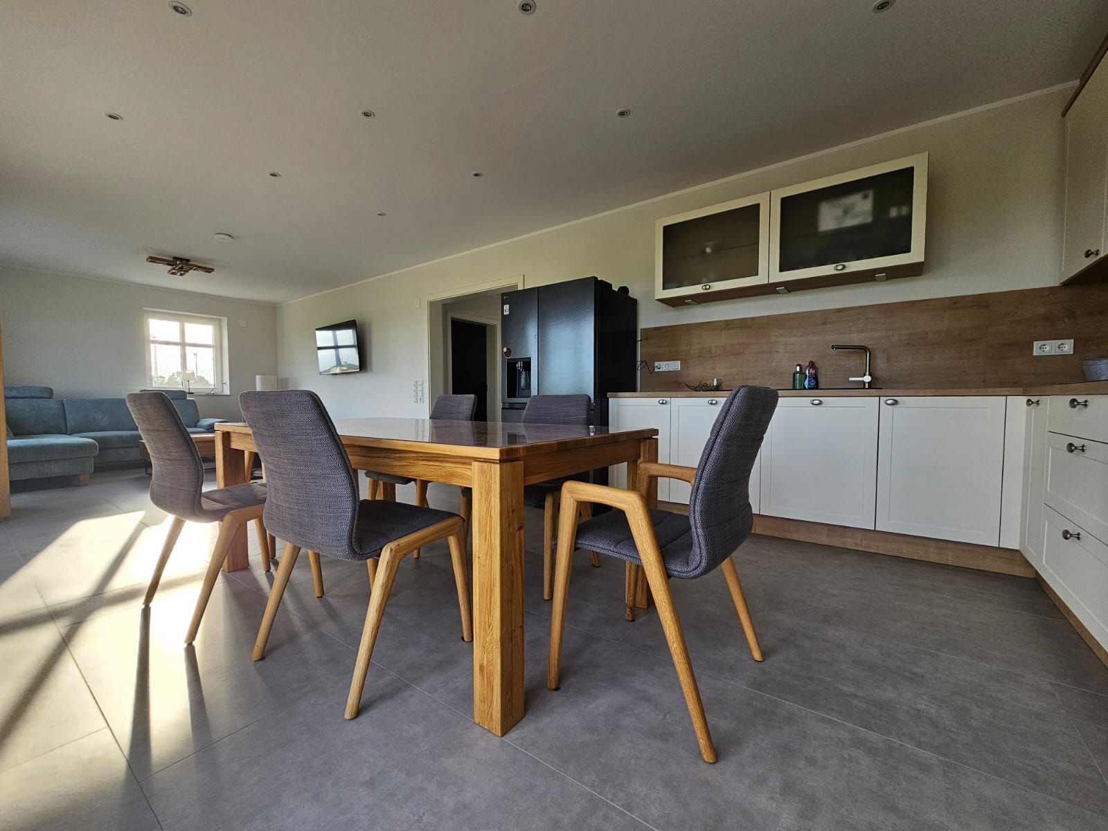 Een moderne keuken met een eettafel en stoelen, een ingebouwde oven en een televisie boven de aanrechten.