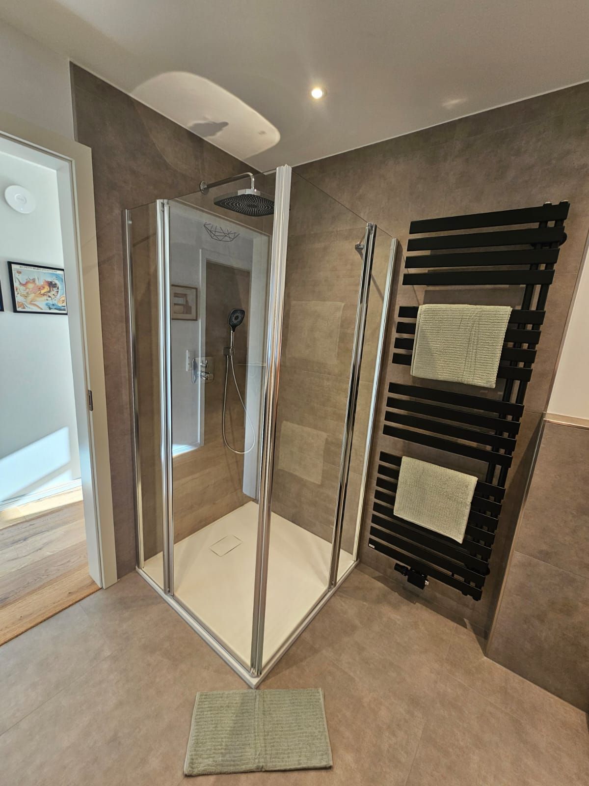 A modern bathroom with a glass-enclosed shower, a towel rack, and a visible showerhead.