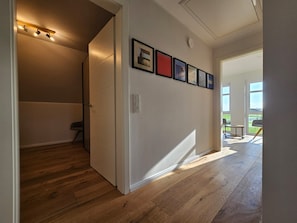 A hallway with wooden flooring, a staircase, and a wall with framed pictures.
