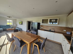 A modern kitchen with a dining area, a sofa, and a TV mounted on the wall.