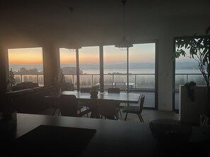 Um interior moderno com grandes janelas, uma área de refeições e vista para o mar.