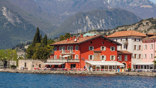 Un hôtel situé au bord de l’eau, composé de plusieurs bâtiments, doté d’une terrasse et offrant une vue sur les montagnes.