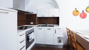 Une cuisine moderne avec des meubles blancs, une cuisinière et un évier. On y trouve une table à manger en bois, accompagnée de chaises.