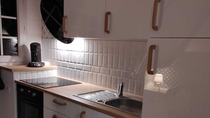 Eine kleine Küche mit weißen Schränken, einem schwarzen Backofen, einer Kaffeemaschine und einem Spülbecken.