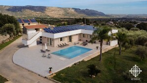En modern villa med pool, solpaneler och utsikt över det omgivande landskapet.