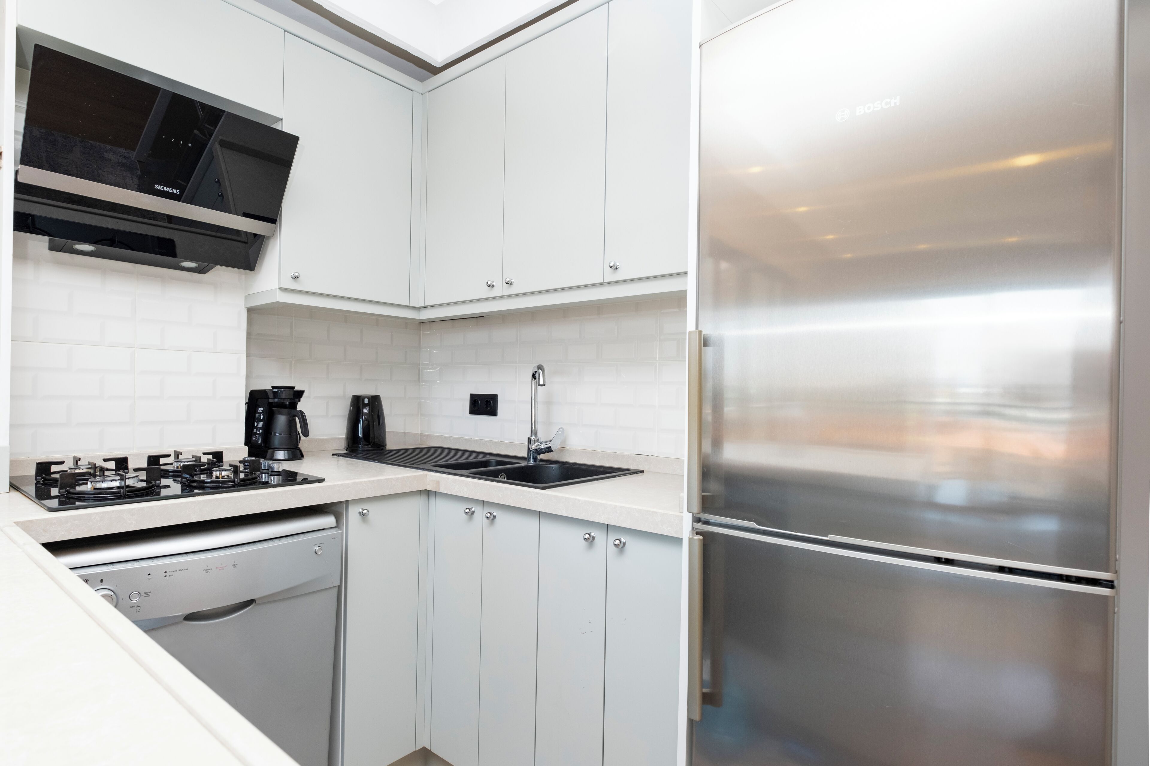 A modern kitchen with white cabinetry, a stainless steel refrigerator, a built-in dishwasher, and a microwave.