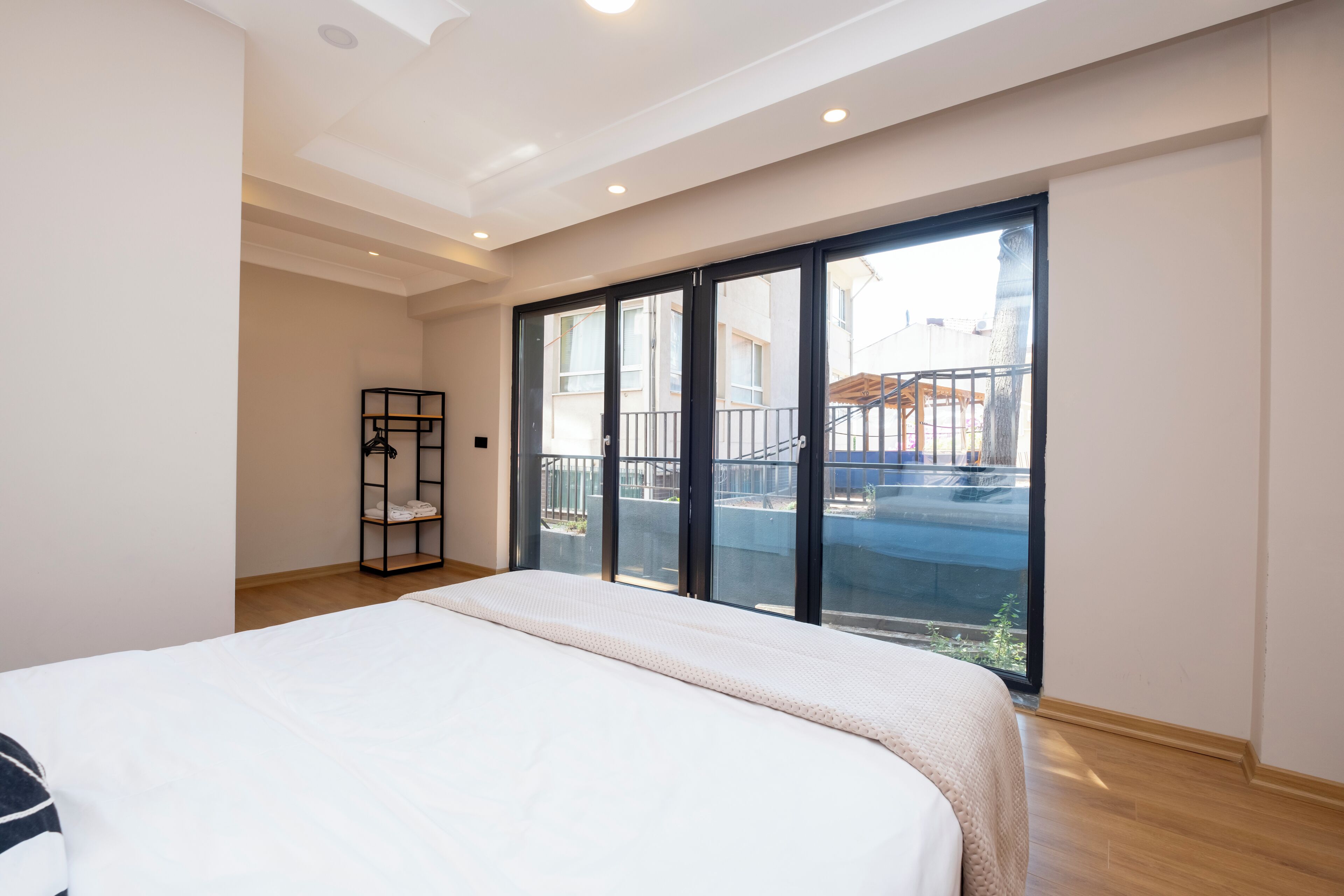 A bedroom with a large bed, a black metal shelf, and a balcony with a railing.