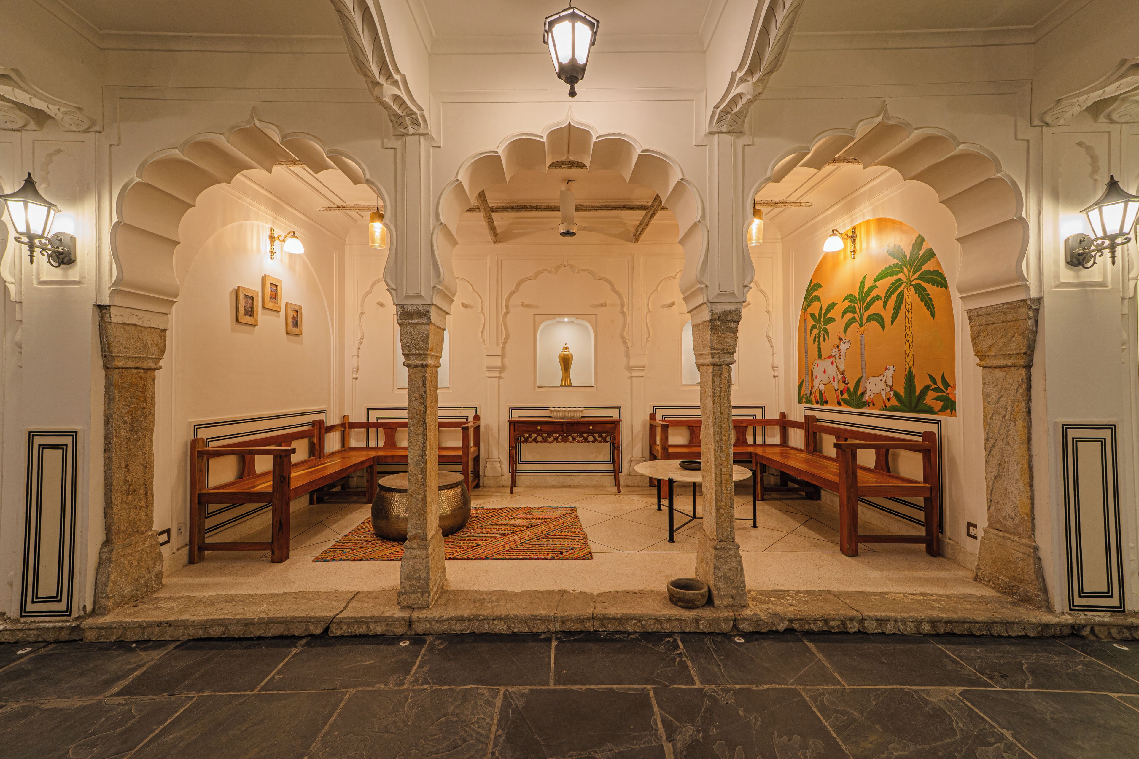 A traditional interior with wooden benches, stone pillars, and a central area with a table and chairs.