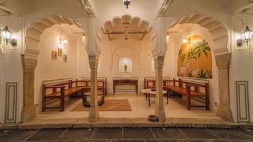 A traditional interior with wooden benches, stone pillars, and a central area with a table and chairs.