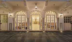 Una entrada tradicional con puertas ornamentales y columnas, que conduce a un comedor con mesas y sillas.