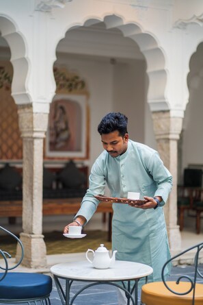 A person serving tea at a table with a white teapot and cup, in a room with arches and a painting on the wall. - Sitaram Bhawan - A 250-Year- Old Heritage Haveli, Jaipur (Jaipur)