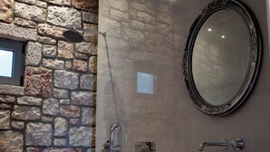 Un bagno con parete in pietra, uno specchio rotondo, un lavandino e un water.