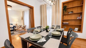 Un coin repas avec une table dressée pour quatre personnes, des chaises, une bibliothèque et un miroir qui reflète la pièce.