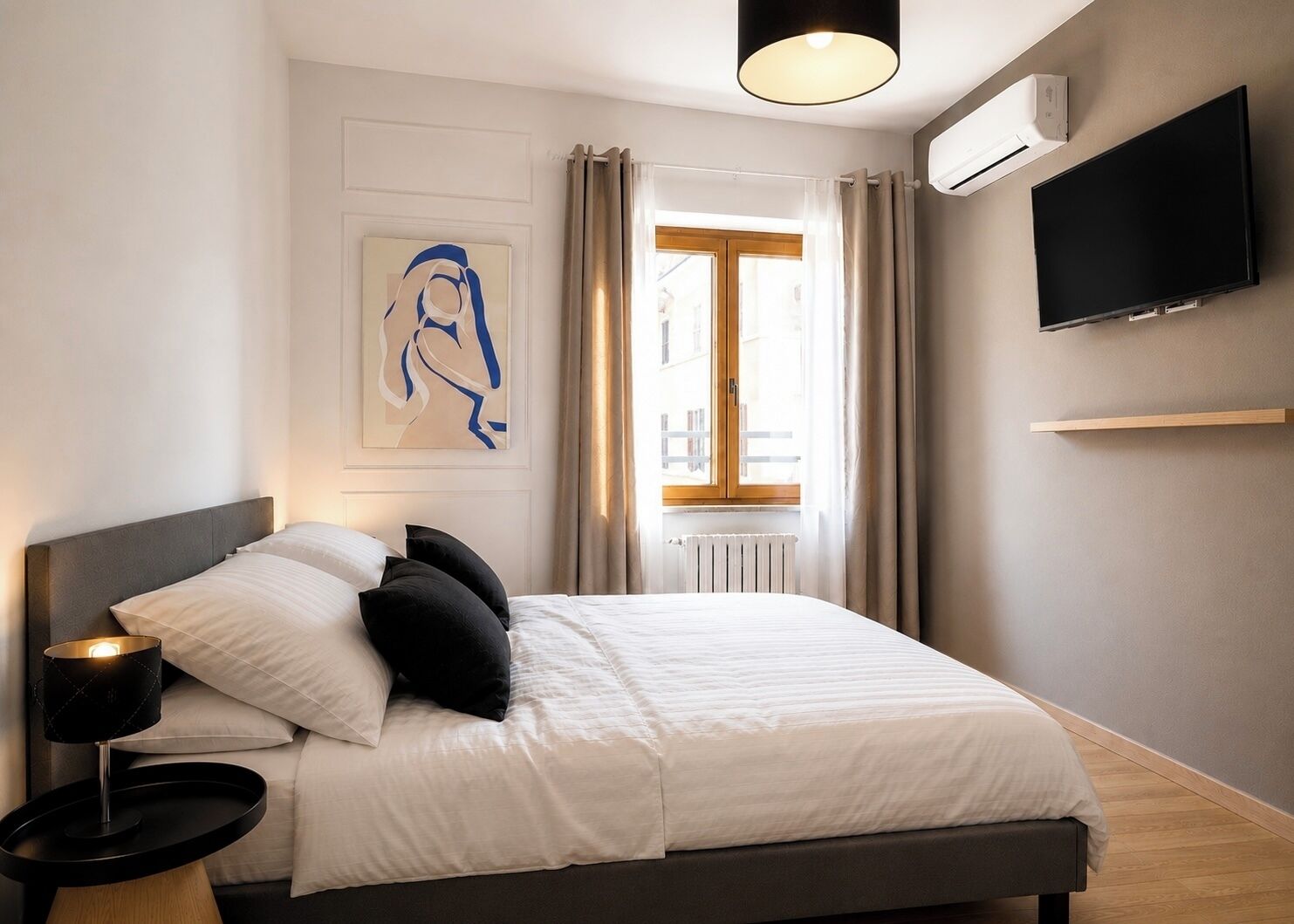 Una camera d'albergo moderna con un letto, una lampada da comodino, una TV a muro e una finestra con tende.