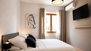 Une chambre d’hôtel moderne équipée d’un lit, d’une lampe de chevet, d’un téléviseur fixé au mur et d’une fenêtre avec des rideaux.