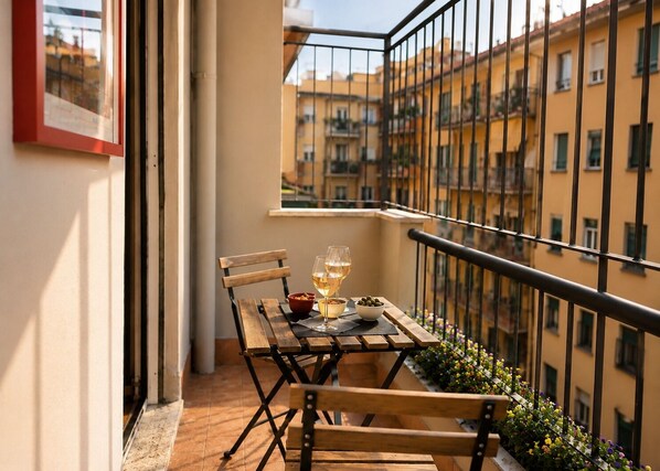 Ein Balkon mit Holztisch, zwei Weingläsern, einer Oliven-Schale und einer kleinen Nuss-Schale.