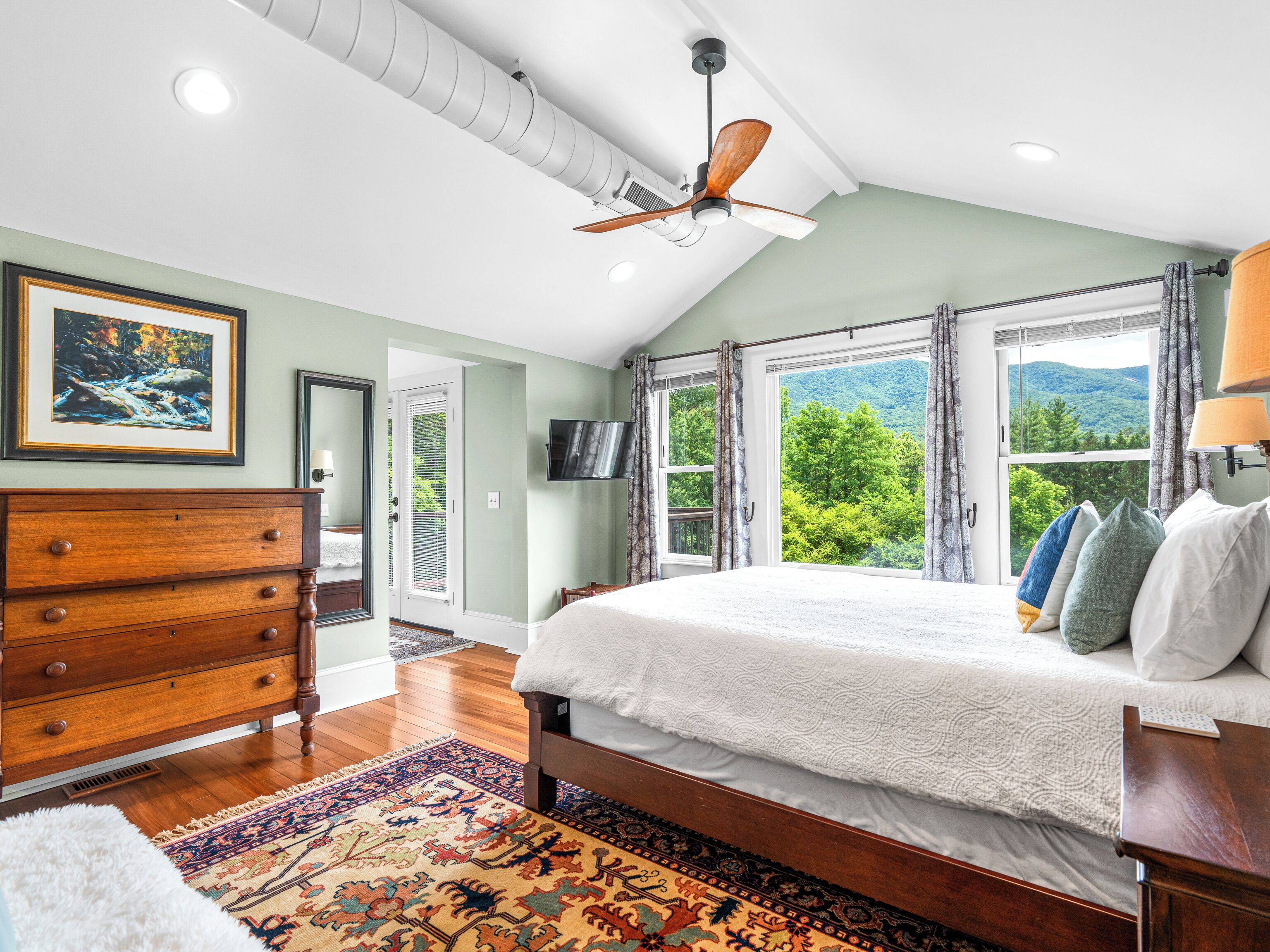 A bedroom with a large bed, a ceiling fan, a TV, and a view of a mountain.