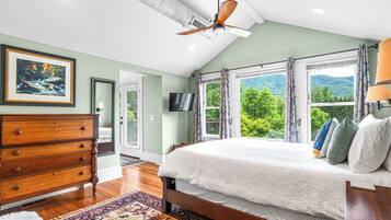 A bedroom with a large bed, a ceiling fan, a TV, and a view of a mountain.