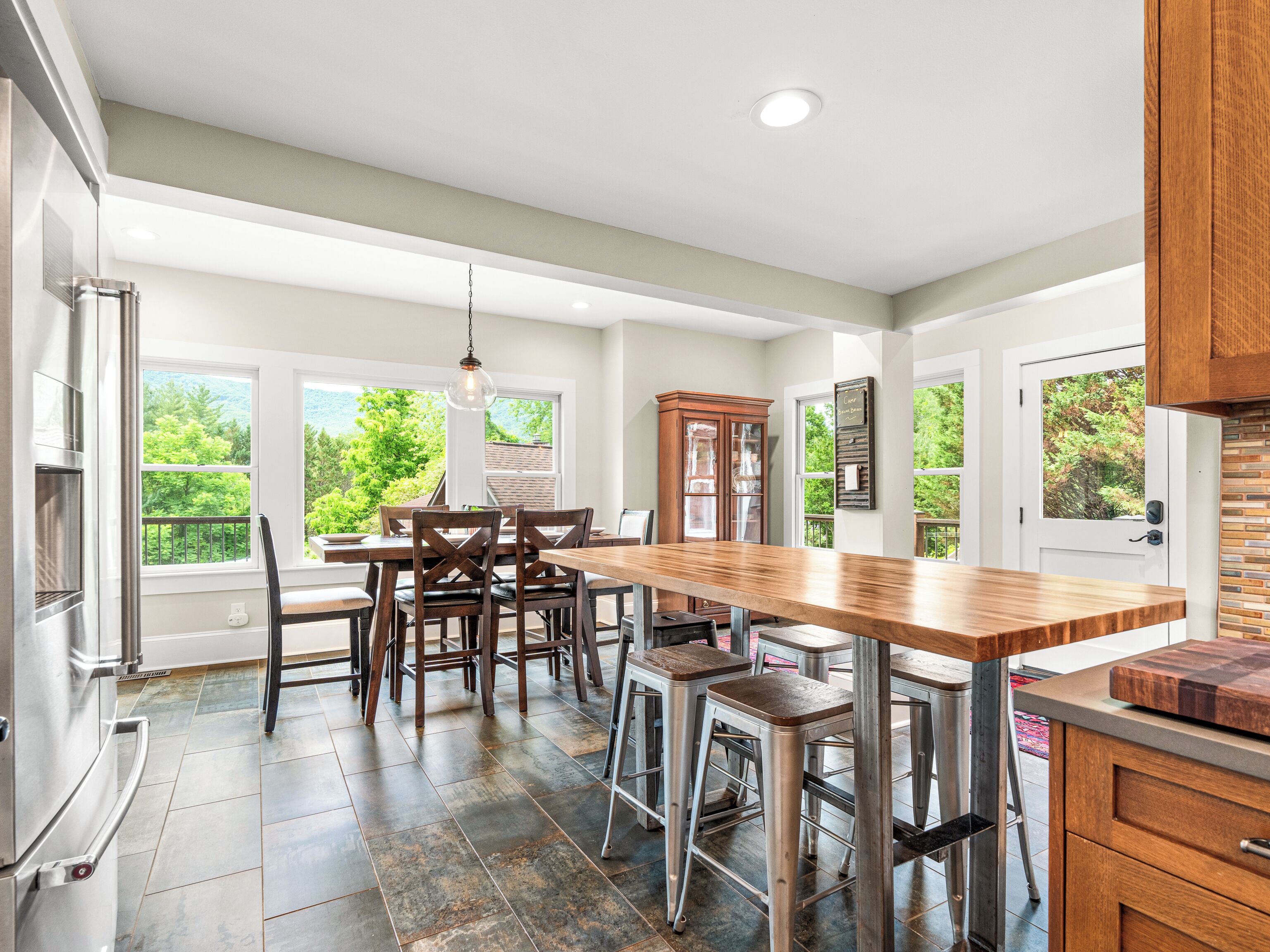A modern kitchen with a large island, bar stools, and a view of greenery outside.