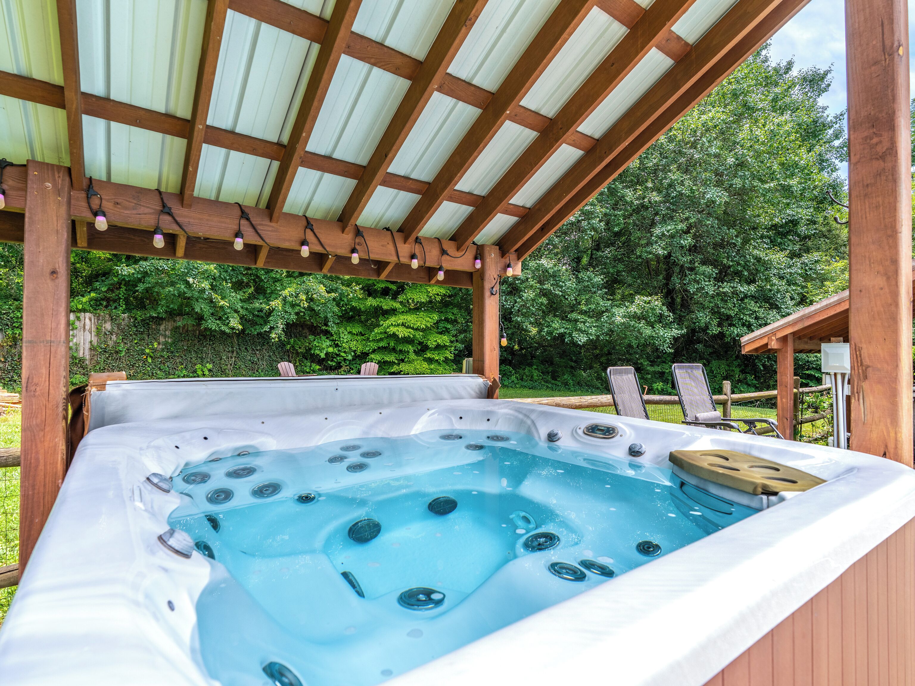 Ein Whirlpool unter einer Hollaube mit Metallverkleidung, umgeben von viel Grün.