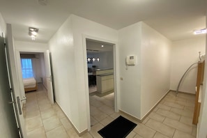 A hallway leading to a bedroom with a bed, a kitchenette, and a bathroom with a shower. - Stylish Apartment with North Sea Views (NIEUWPOORT)