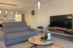 A modern living room with a grey sofa, a round coffee table, a flat-screen TV, and pendant lights. - Stylish Apartment with North Sea Views (NIEUWPOORT)