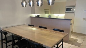 Een moderne keuken met een centraal eiland, hanglampen, en een eethoek met een lange tafel en stoelen.