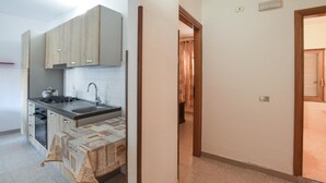 A kitchen with a stove, sink, and cabinets. There is a table with a tablecloth and a chair. A hallway leads to another room. - Lovely apartment in Ricadi with WiFi (Ricadi)