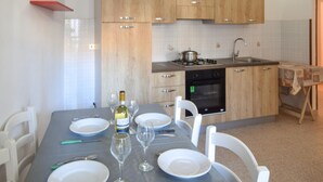 A kitchen with wooden cabinets, a gas stove, an oven, and a sink. There is a dining table set with plates, glasses, and cutlery. - Lovely apartment in Ricadi with WiFi (Ricadi)