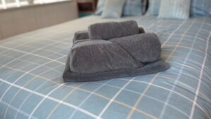 A bed with a blue checkered bedspread and two rolled-up towels. - Welcome Retreats (Plymouth)
