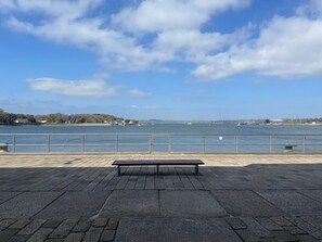 A waterfront promenade with a bench, a railing, and a view of the sea and distant buildings. - Welcome Retreats (Plymouth)