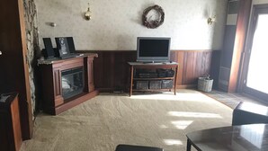 Un salon avec une cheminée, un téléviseur et une table en verre.