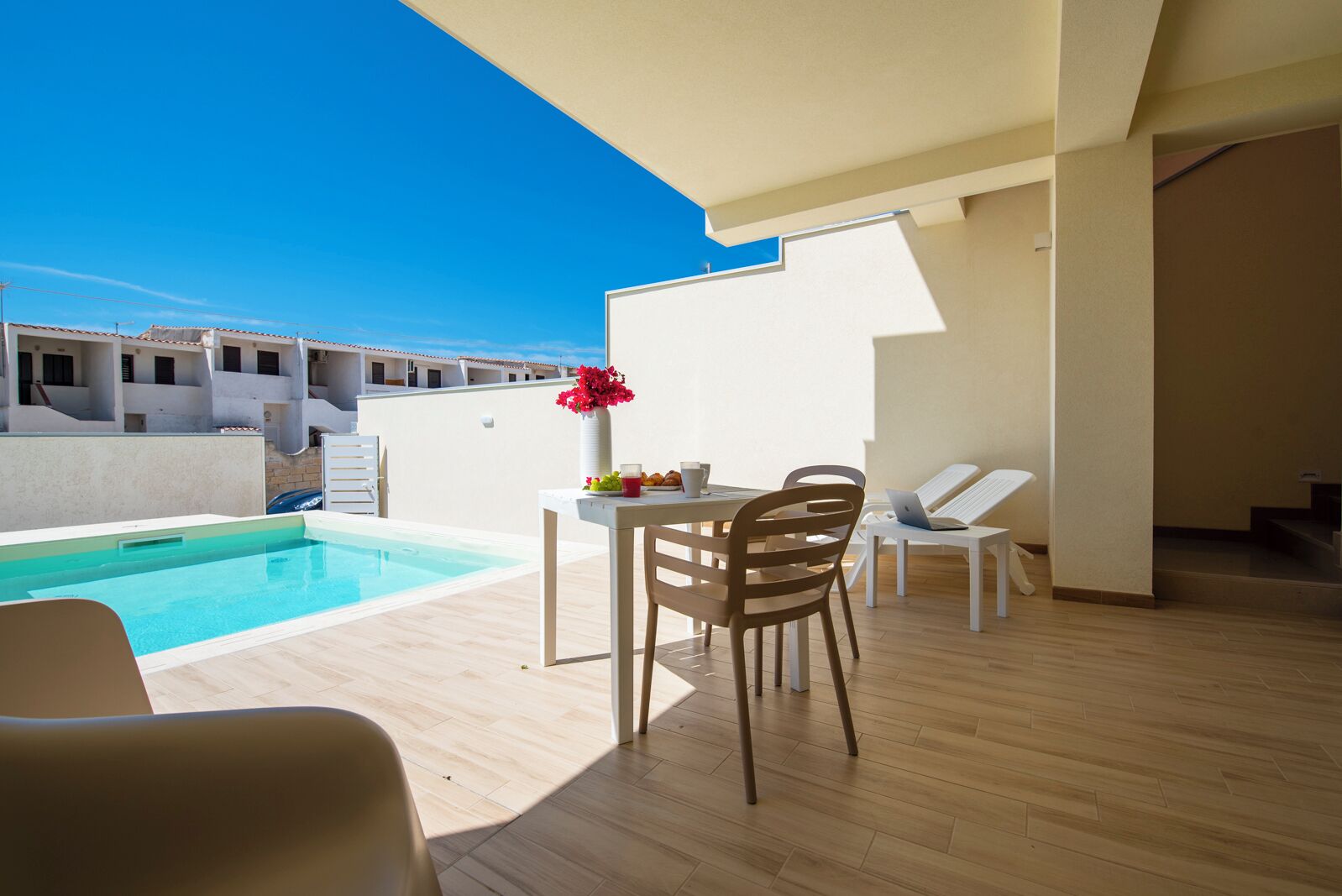 Un espacio al aire libre moderno con piscina, una mesa con sillas y un ordenador portátil.