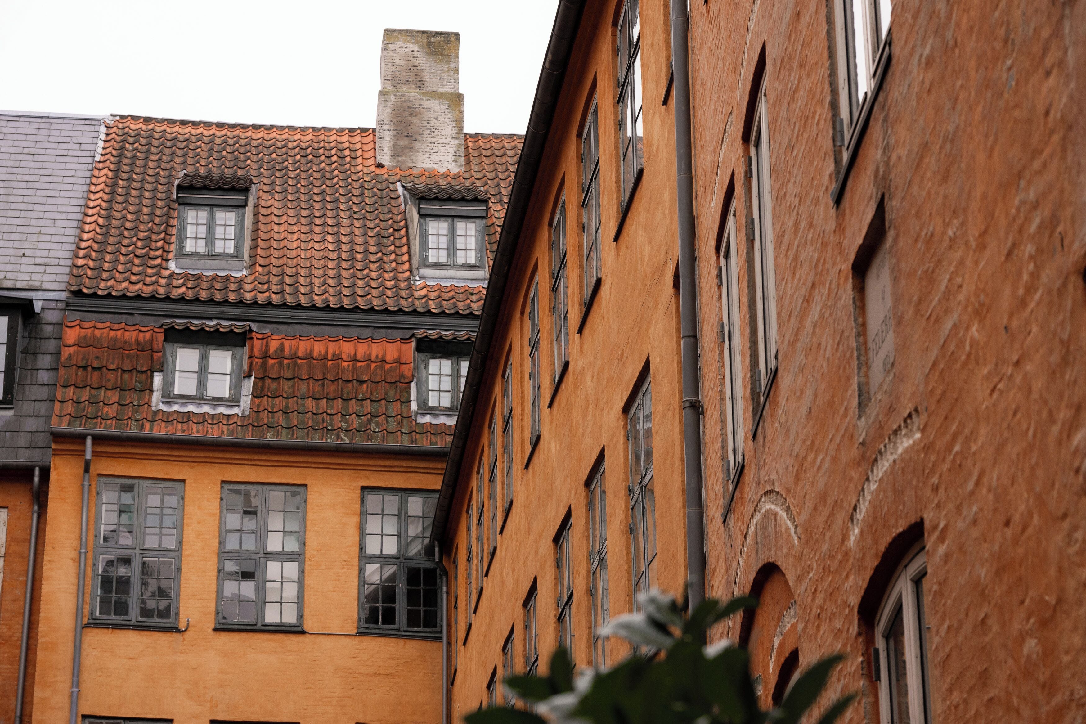 A narrow street with buildings featuring traditional architecture, including a brick facade and a tiled roof.