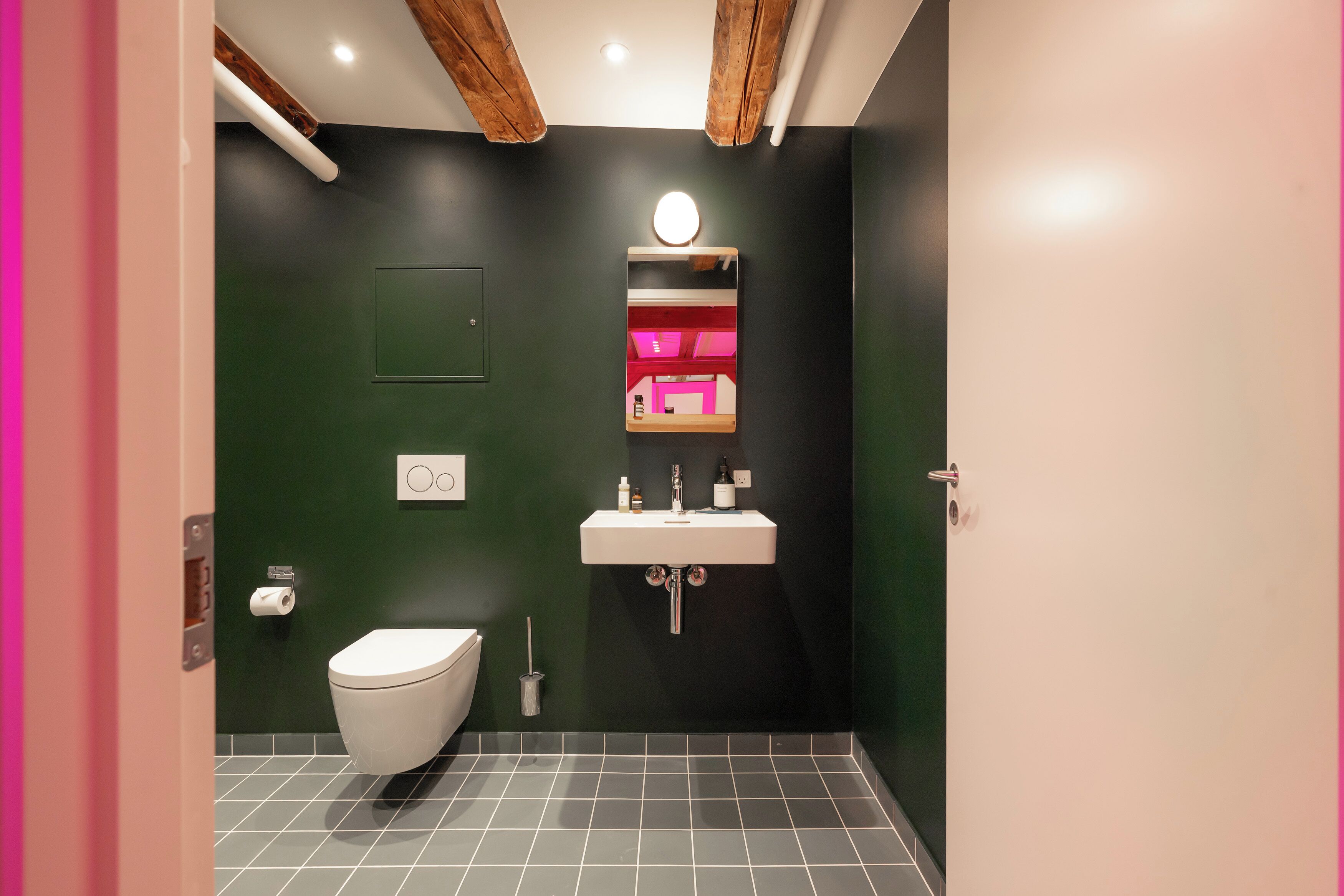 A bathroom with a white toilet, a sink with a mirror, and a green wall.