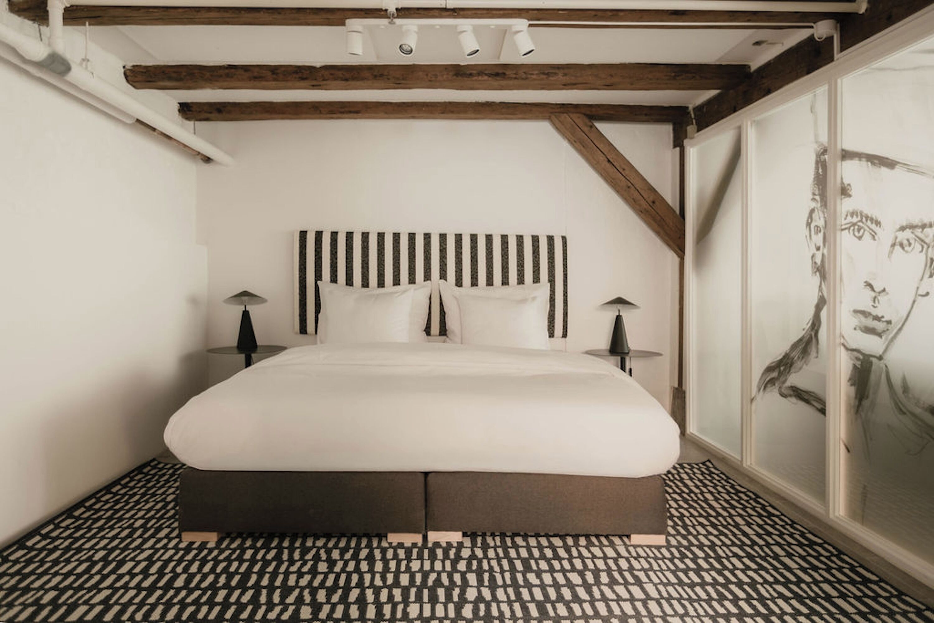 Un dormitorio con cama, dos mesitas de noche, cabecero y suelo estampado.
