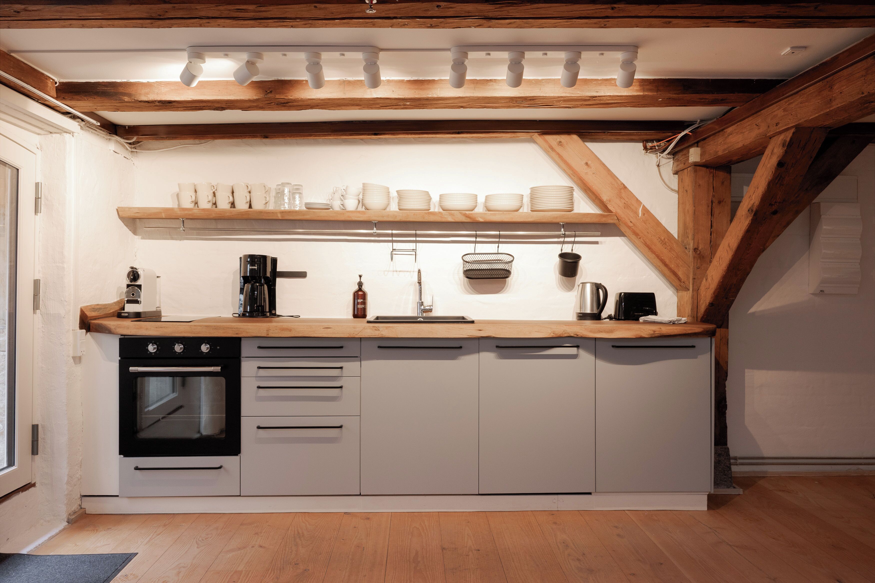 Una cucina compatta con travi in legno, mobili bianchi e forno integrato.
