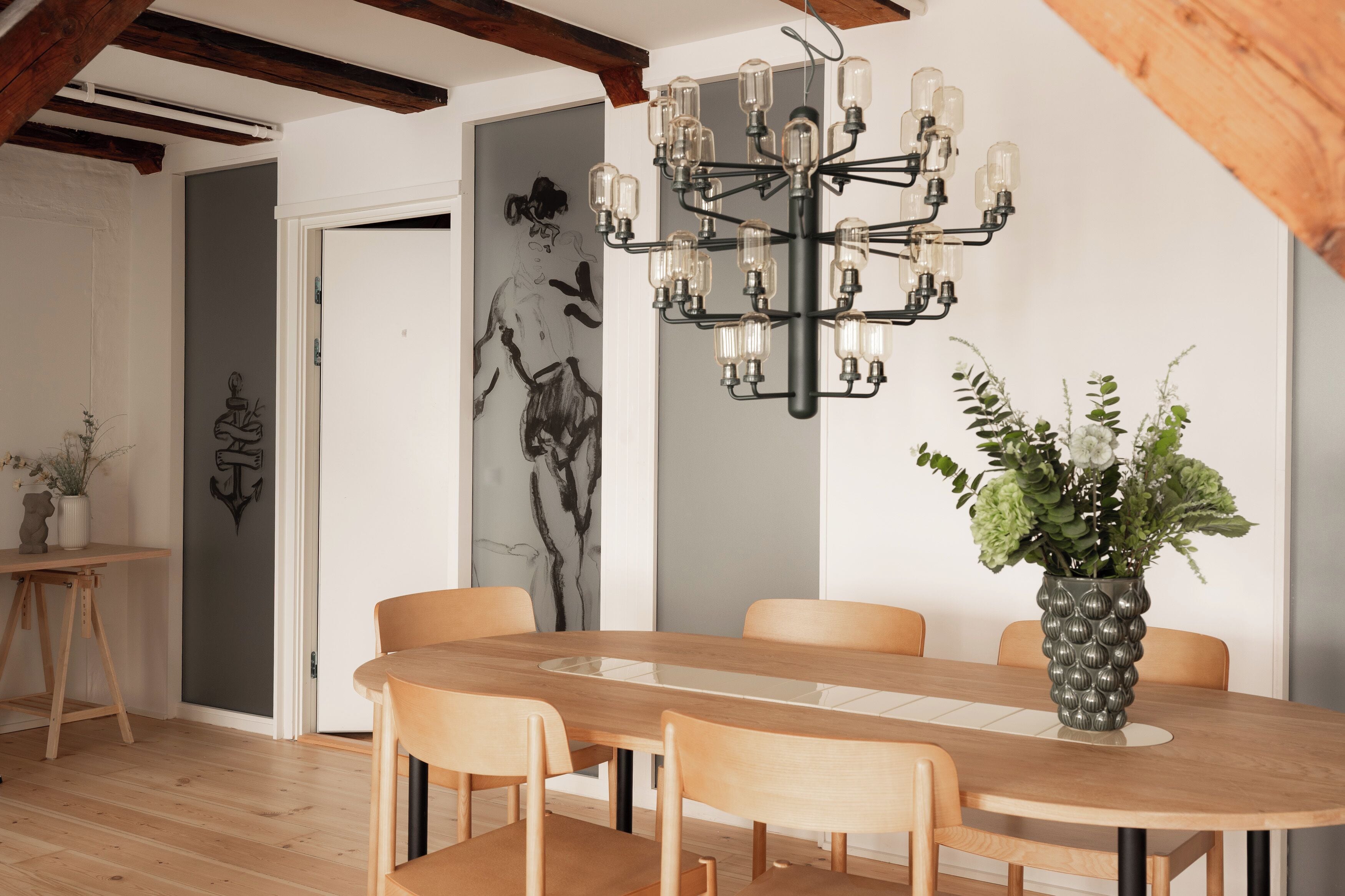 A dining area with a wooden table, chairs, a chandelier, and a vase with flowers.