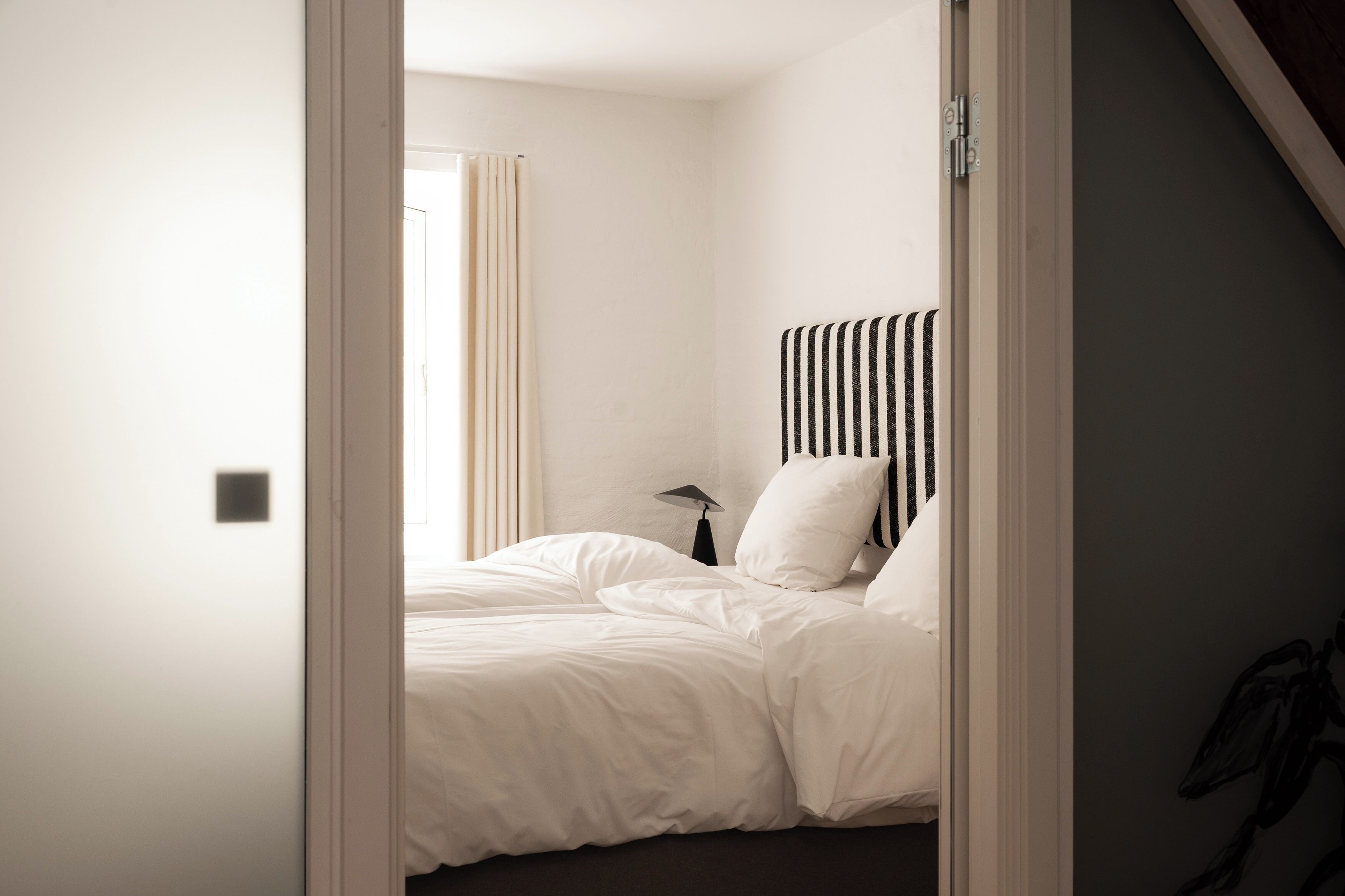 Un dormitorio con cama, mesita de noche, lámpara y ventana con cortinas.