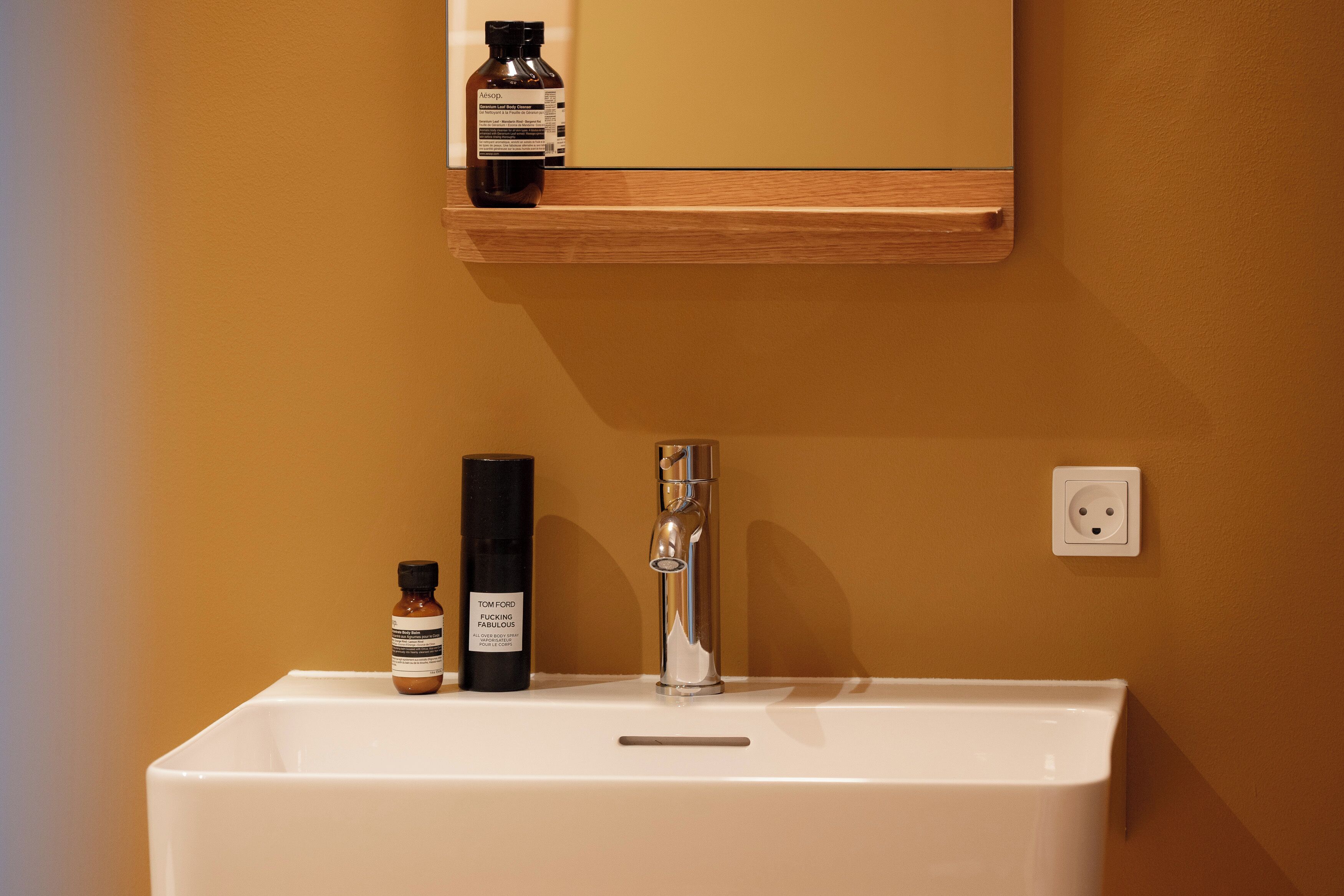A bathroom with a white sink, a mirror above it, and two bottles of Tom Ford perfume on the shelf.