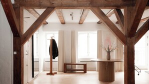 A spacious room with wooden beams, a round wooden table, a bench, and a coat rack. - Nyhavn43 Suites by Daniel&Jacob's (Copenhagen)