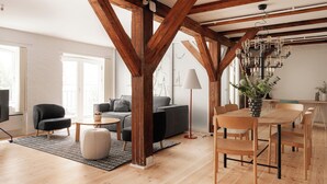 A spacious living area with wooden beams, a dining table with chairs, a sofa, a coffee table, and a lamp. - Nyhavn43 Suites by Daniel&Jacob's (Copenhagen)