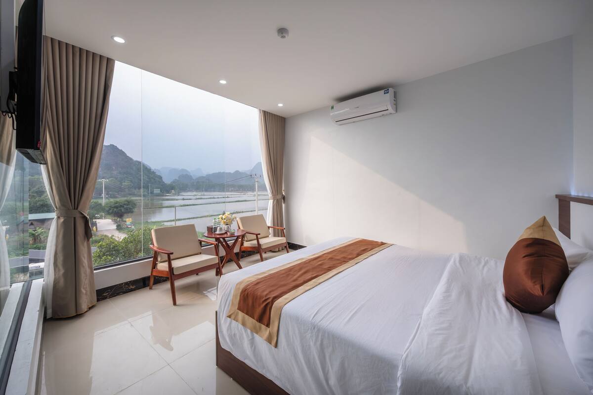 A hotel room with a bed, a TV, a desk with a chair, and a view of the outdoors.
