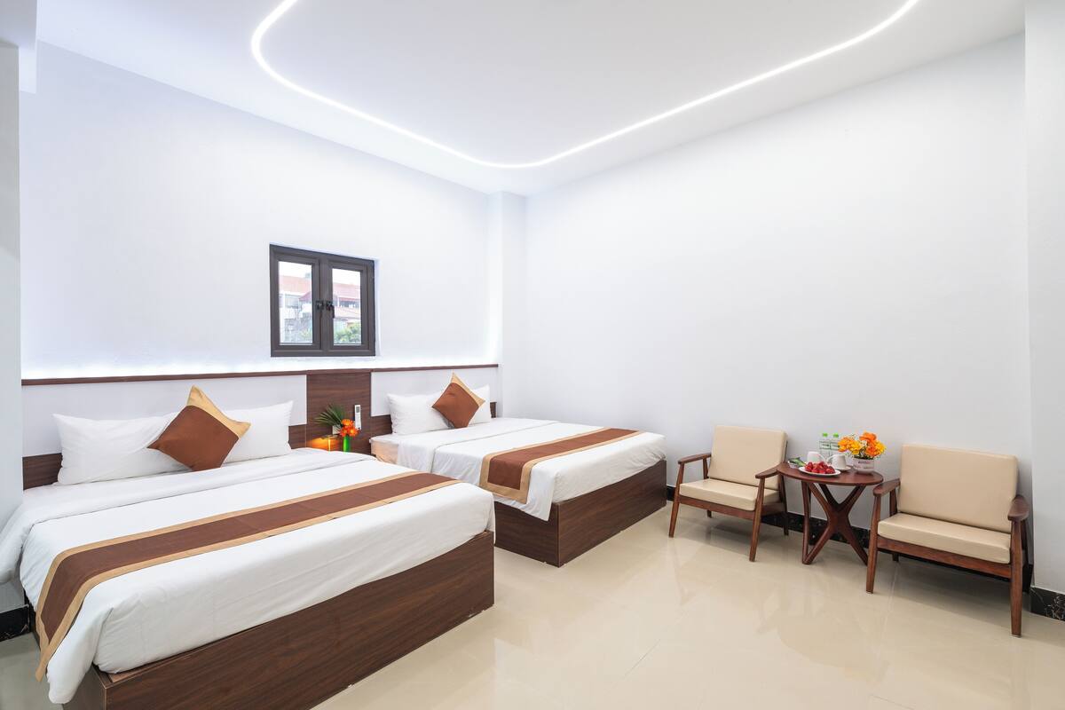 A hotel room with two beds, a small table with fruit, and a chair.