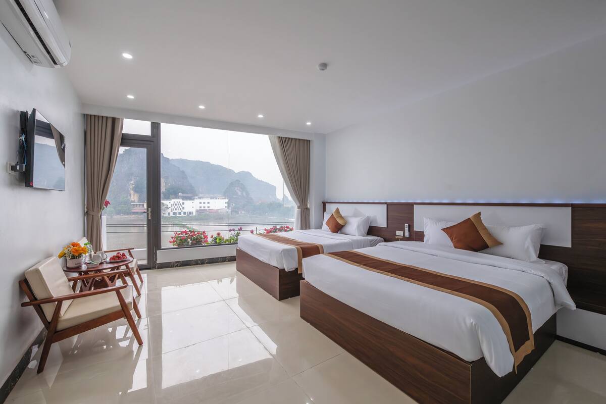 A hotel room with two beds, a TV, a desk with a chair, and a view of mountains.