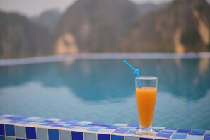 Et glas appelsinjuice med sugerør på en fliserede poolkant.