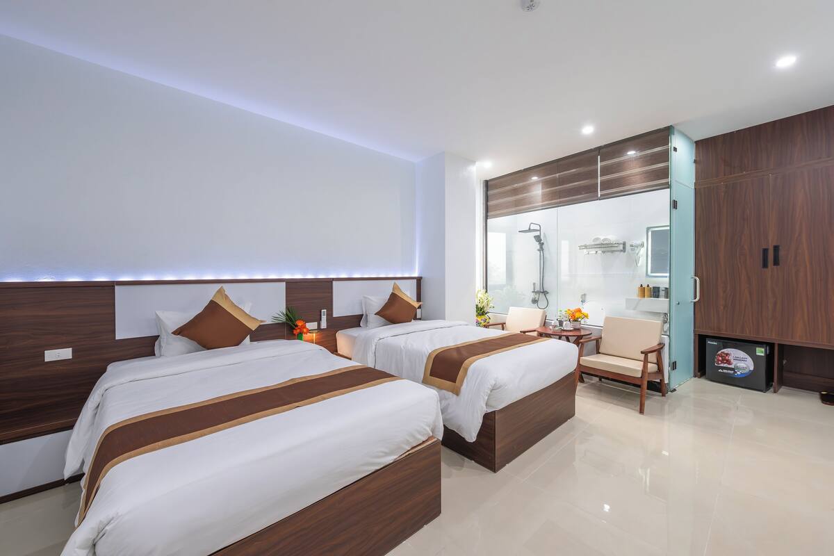 A hotel room with two beds, a sitting area, and a bathroom with a shower.