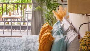 Une chambre à coucher avec un lit, des rideaux, une lampe, une plante en pot et une vue sur la verdure à l’extérieur.