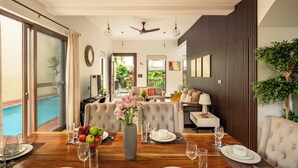 Un coin repas avec une table en bois, des chaises et un vase rempli de fleurs. On peut apercevoir une piscine à travers les portes vitrées.