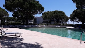 Ein Poolbereich mit Liegestühlen, blauem Himmel und Bäumen.